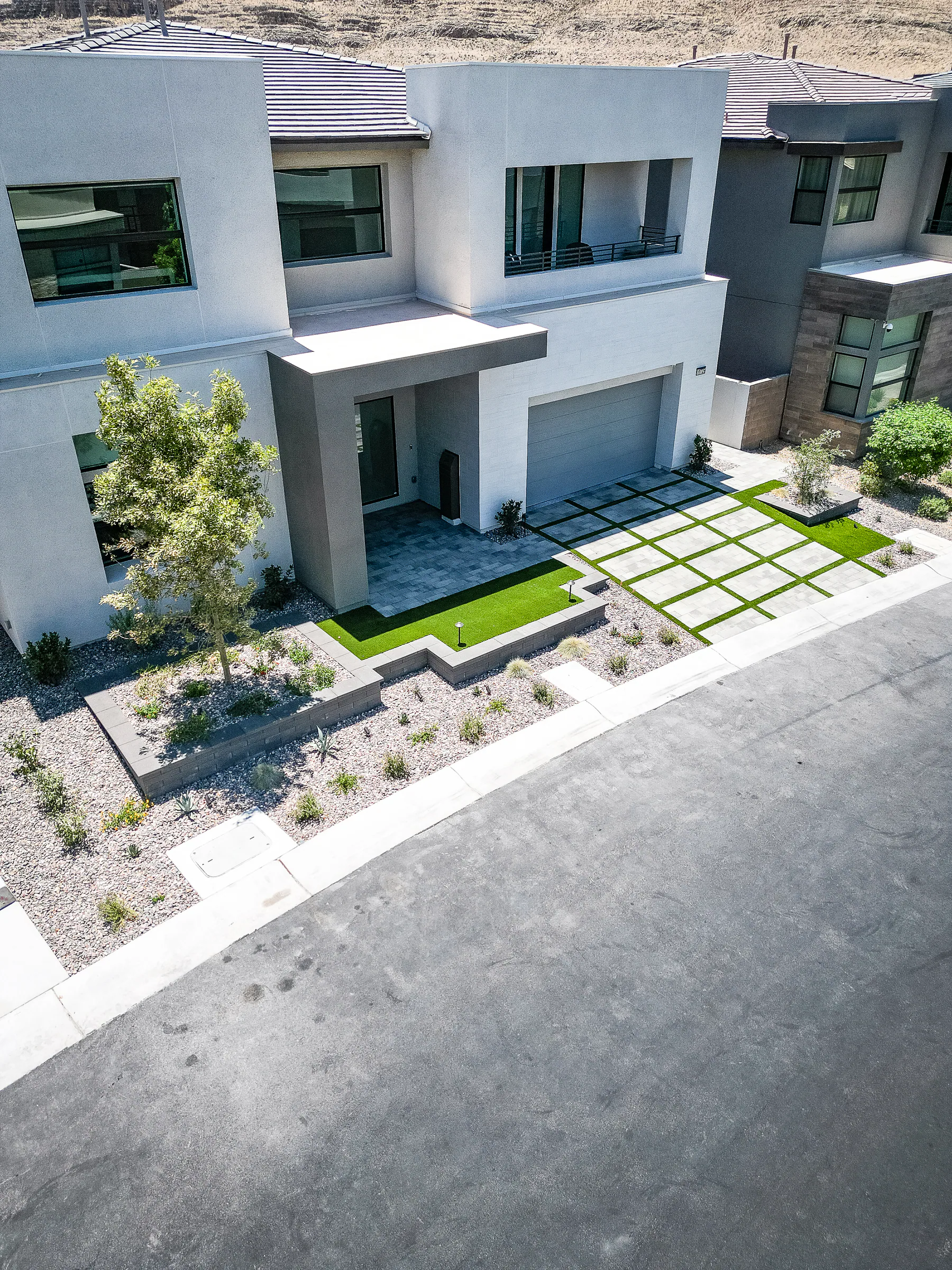 Angled drone view of the house front, turf patch, and paver driveway grid