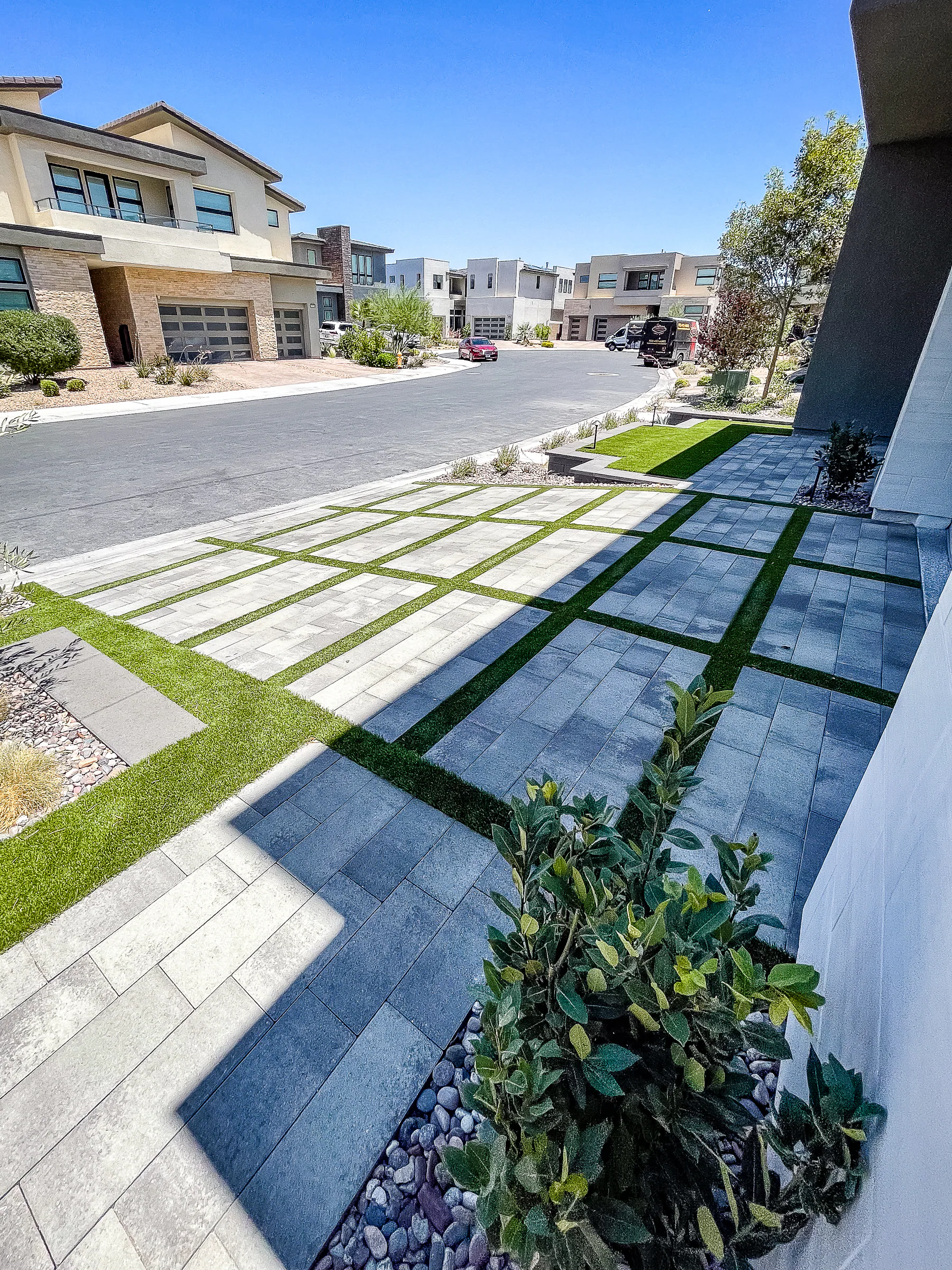 Turf-striped paver driveway angling toward the street beside a shrub planter