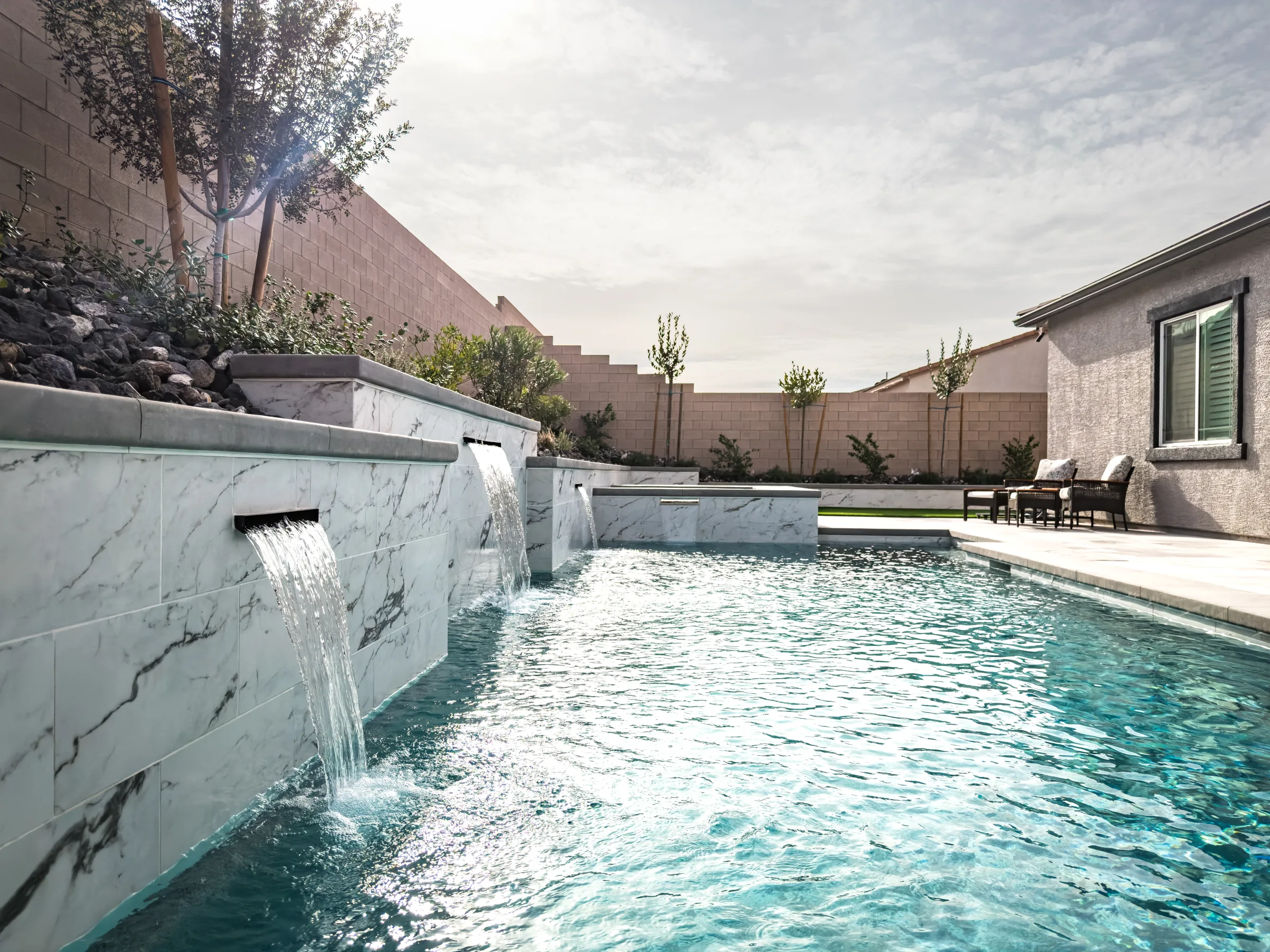 Pool with sheer scupper waterfalls beside a sunlit home