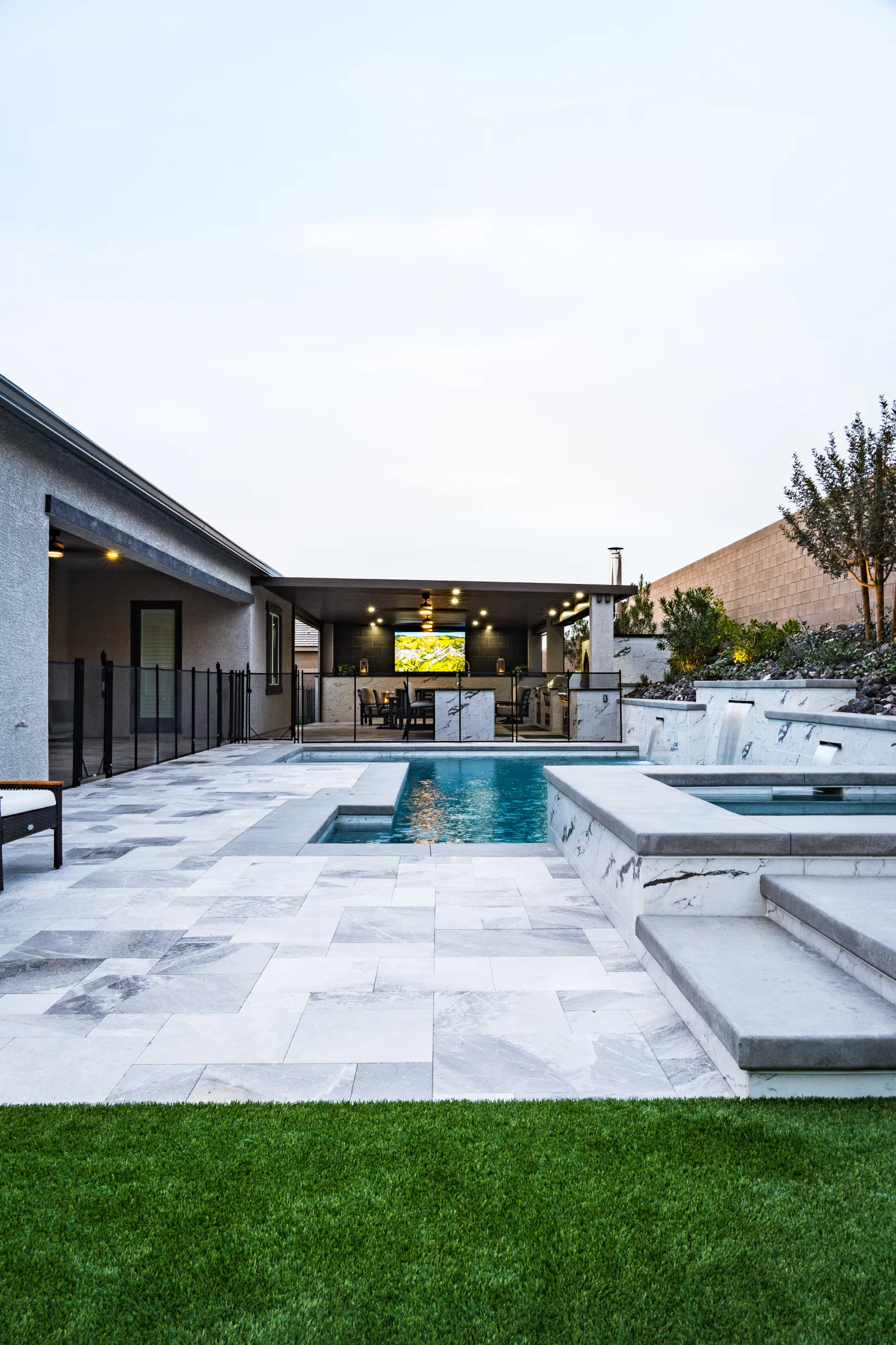 Wide backyard pool, spa, pavilion, and turf at dusk
