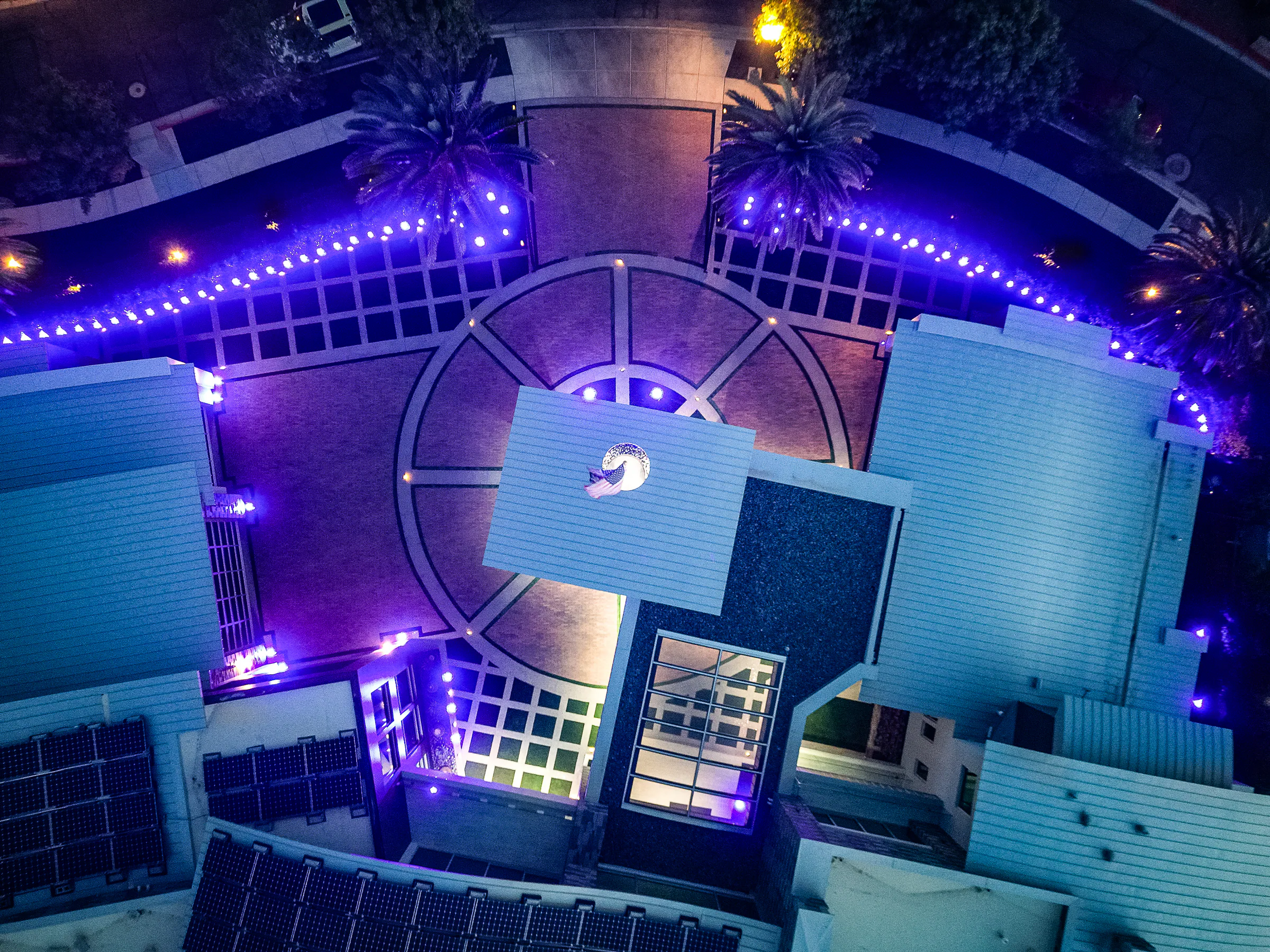 Top-down aerial view of the circular motor court and curved porte cochere illuminated after dark