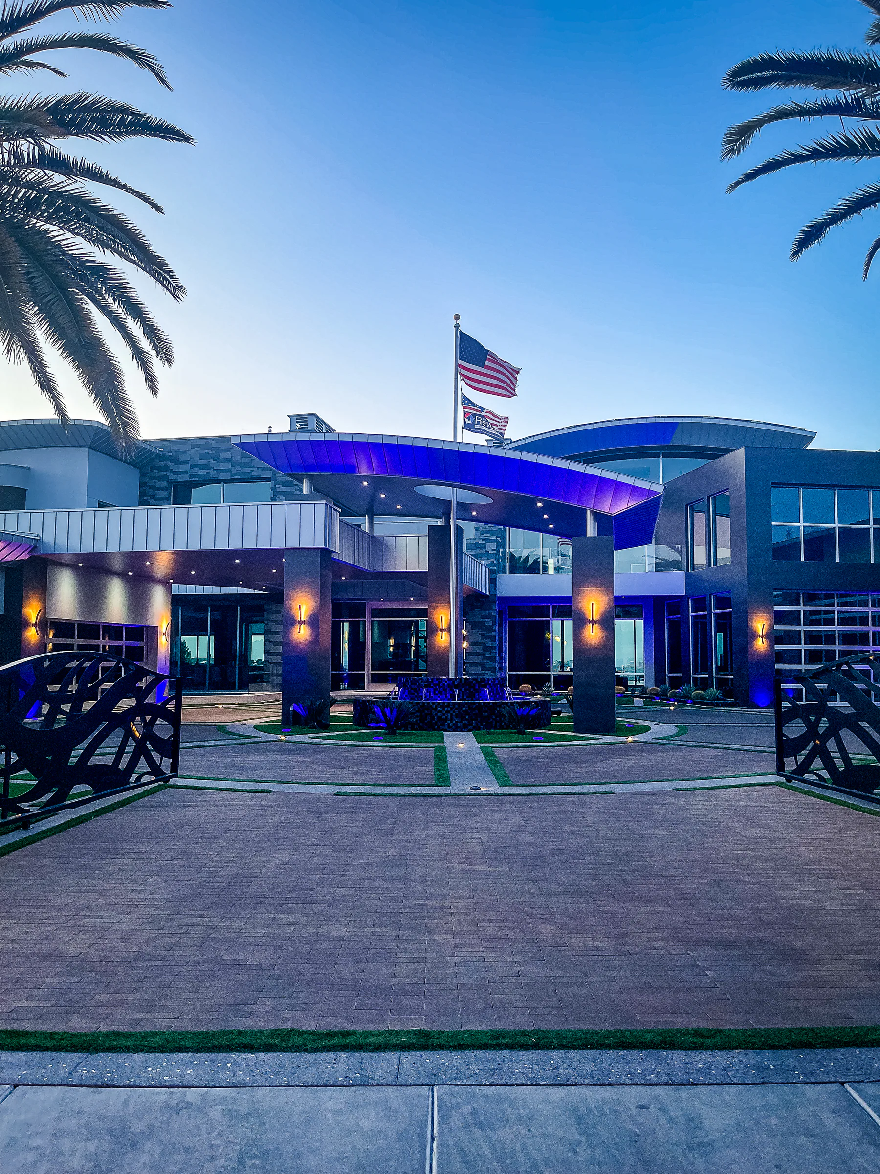 Wide front view of the illuminated estate entrance, motor court, and American flag at dusk