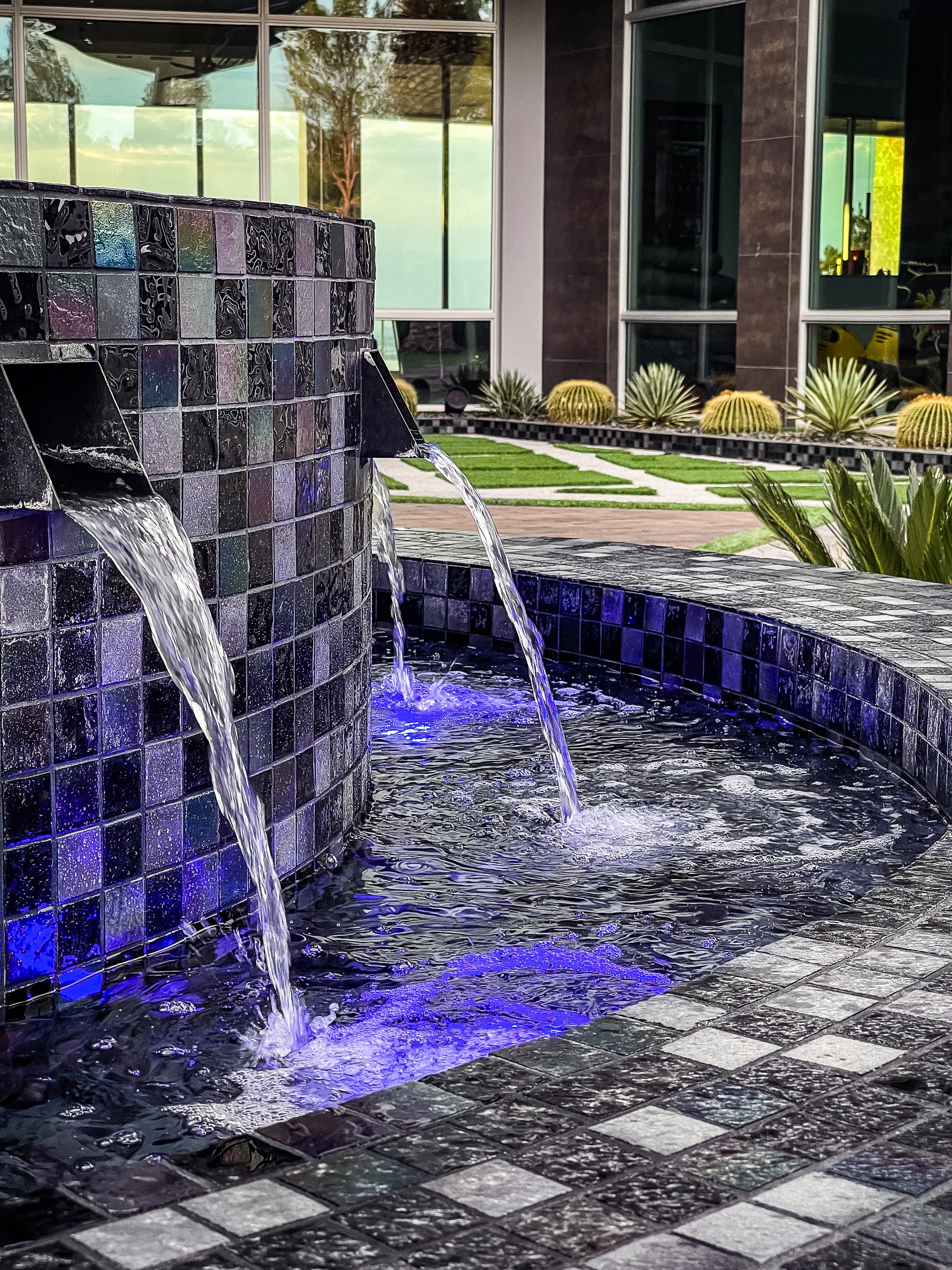 Two scupper waterfalls flowing from the black-tiled fountain wall into the basin