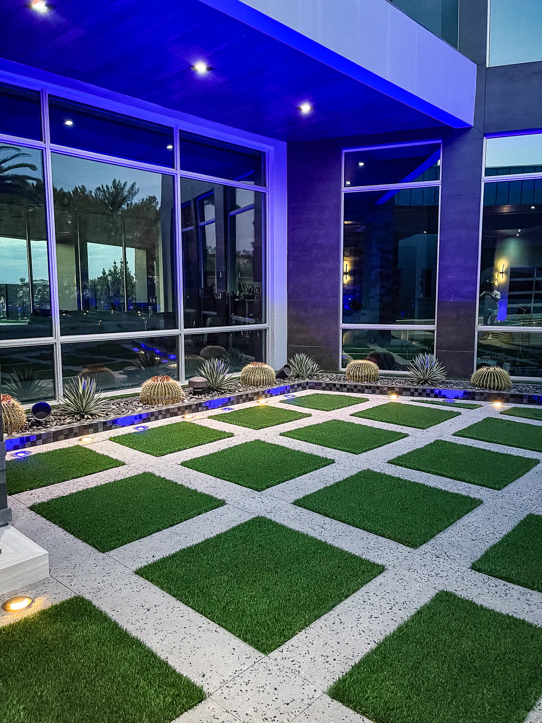 Geometric turf and concrete pattern beside the glass facade and barrel cactus planting