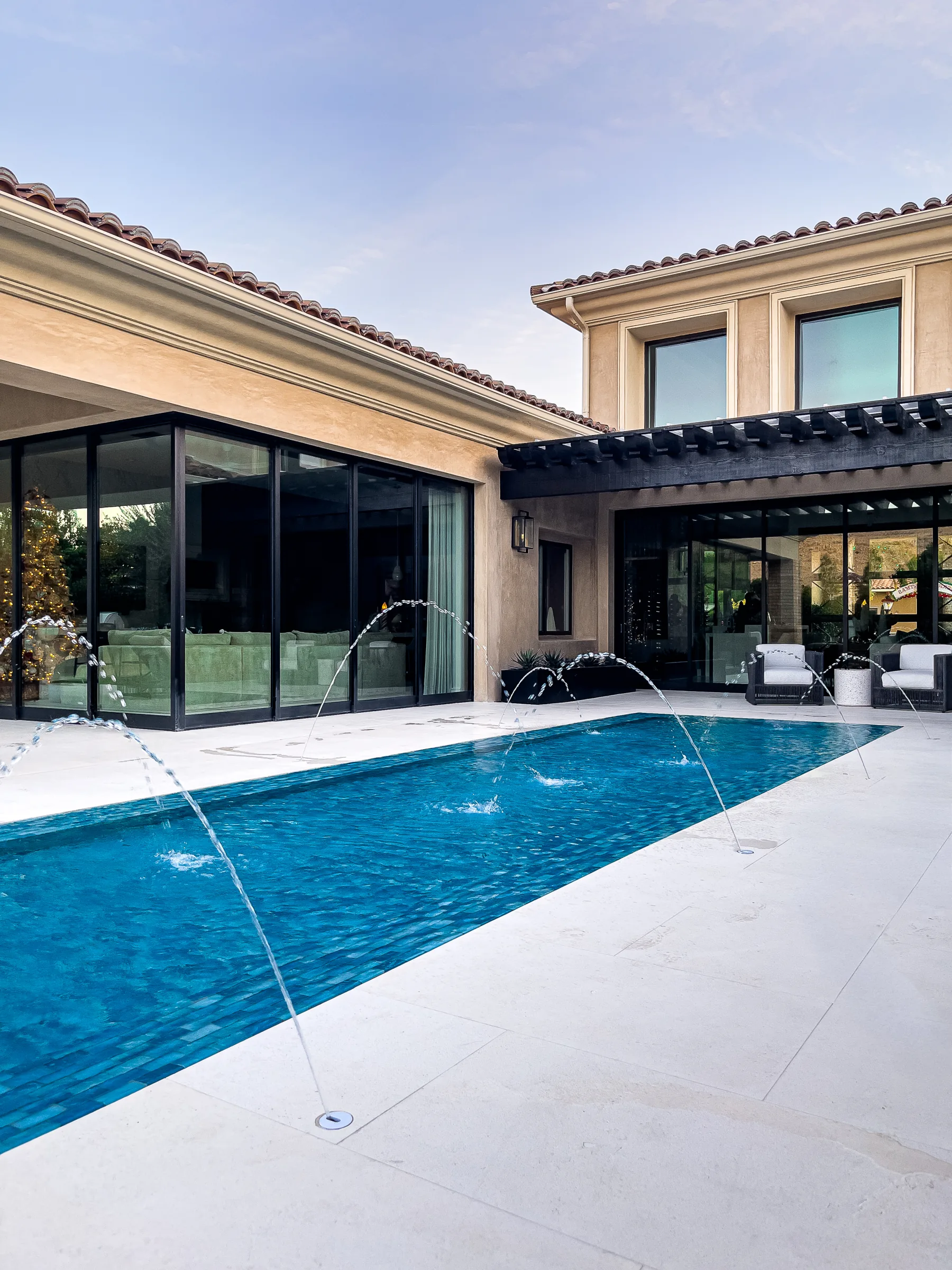 Wide pool deck and jets beside a glass-walled home