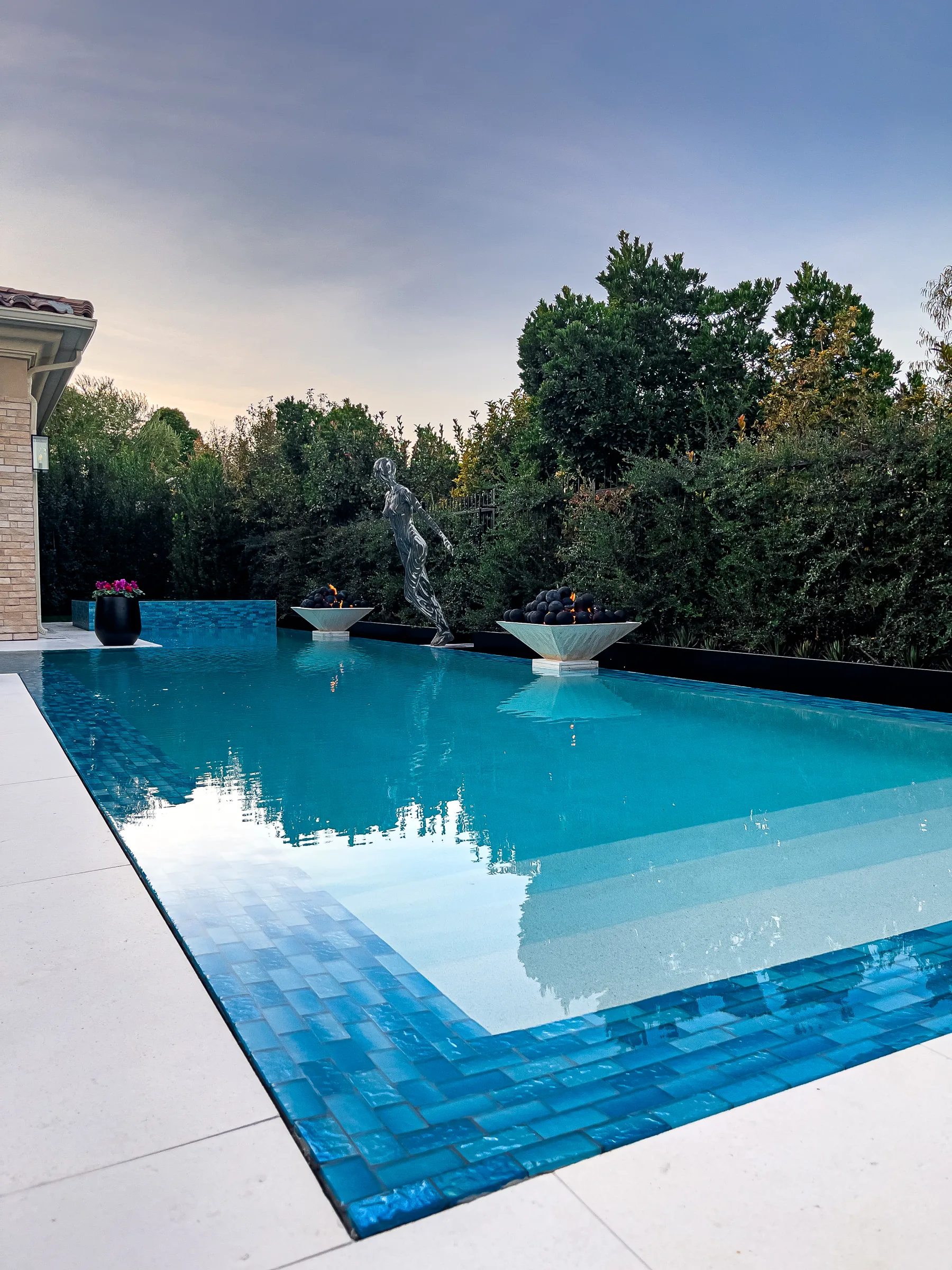 Infinity-edge pool with blue tile, fire bowls, and a statue