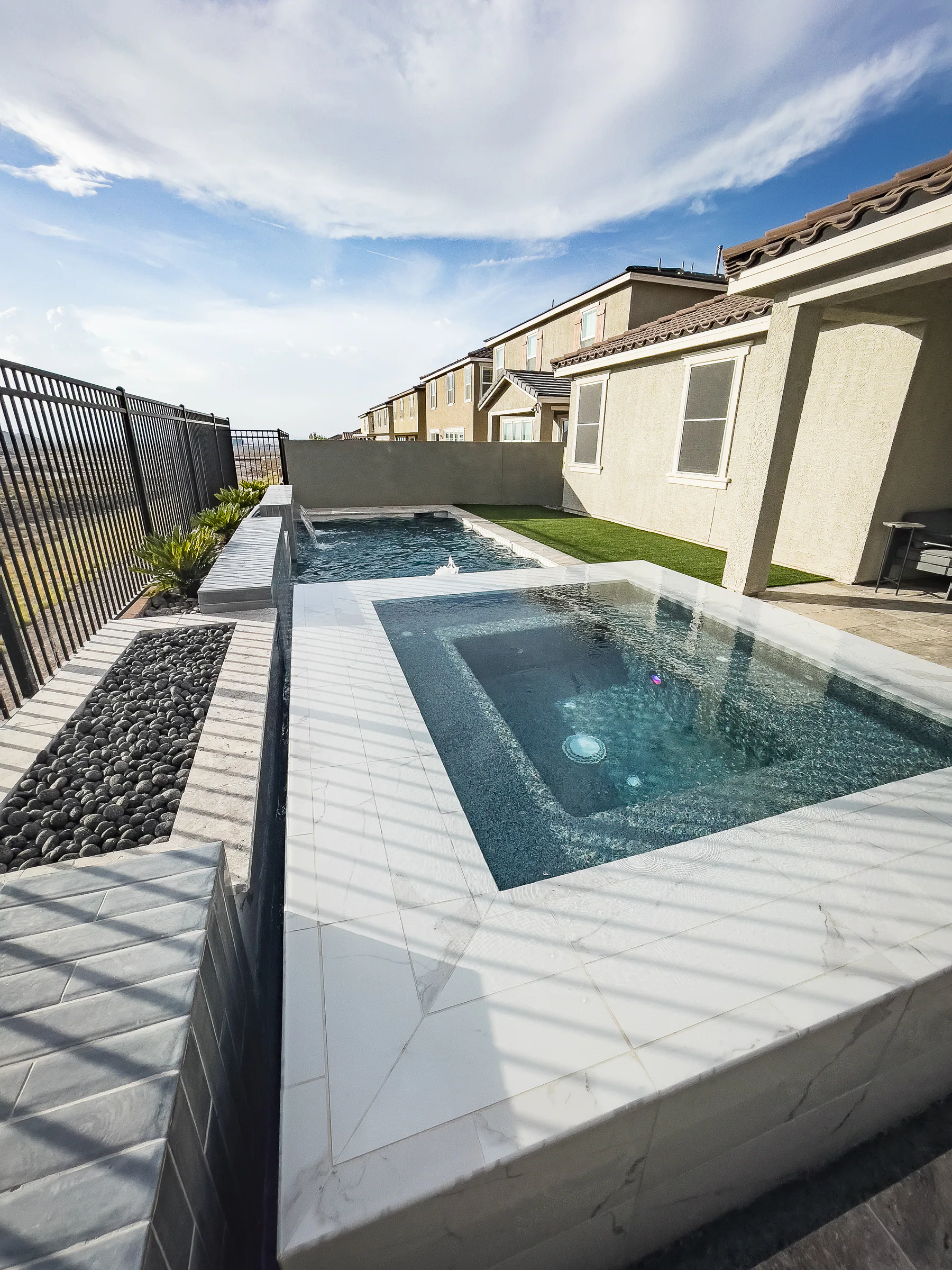 Geometric pool and raised spa extending along a compact backyard with turf and stone paving