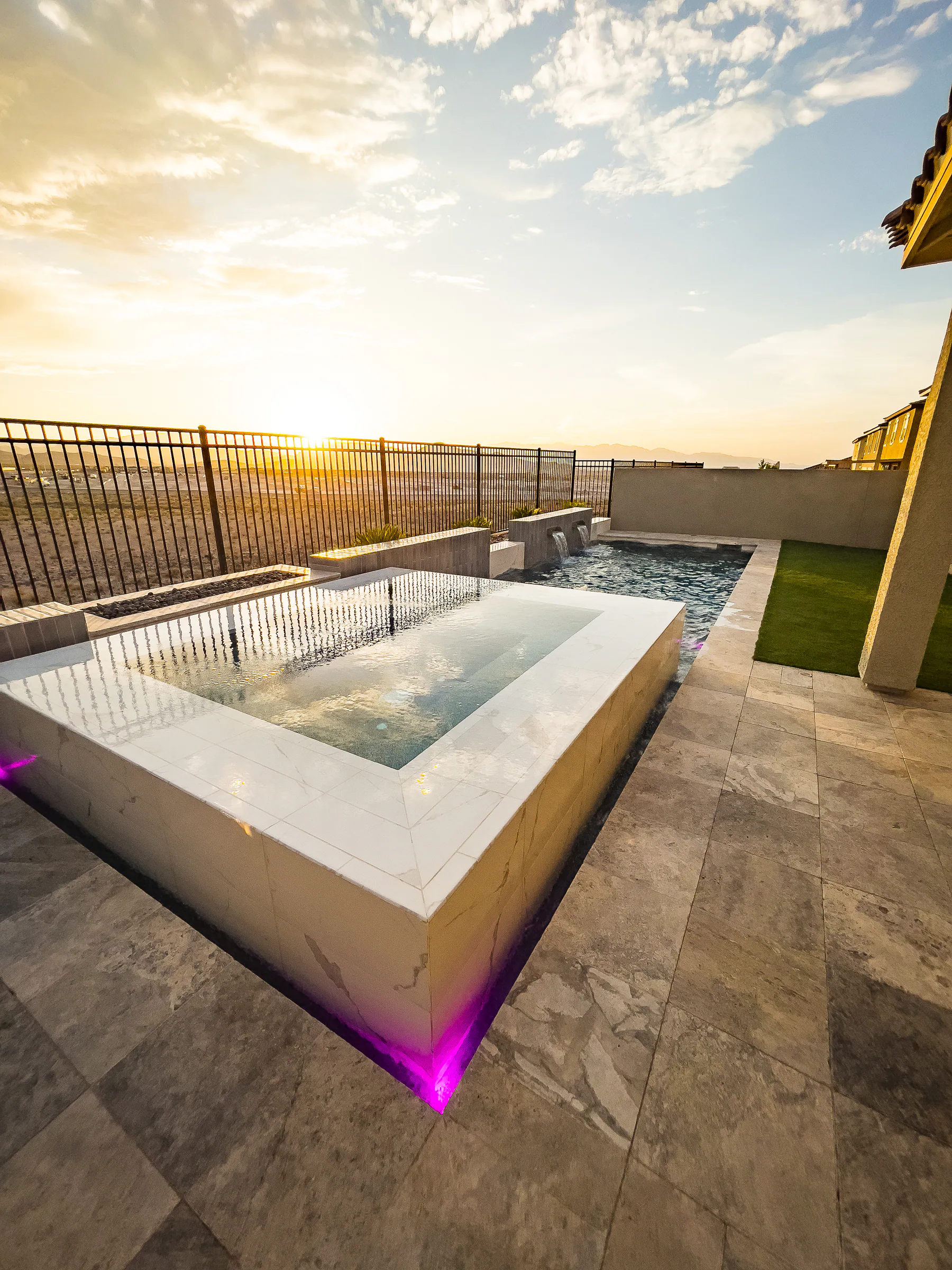 White-tiled raised spa spilling over a glass edge into the pool at sunset