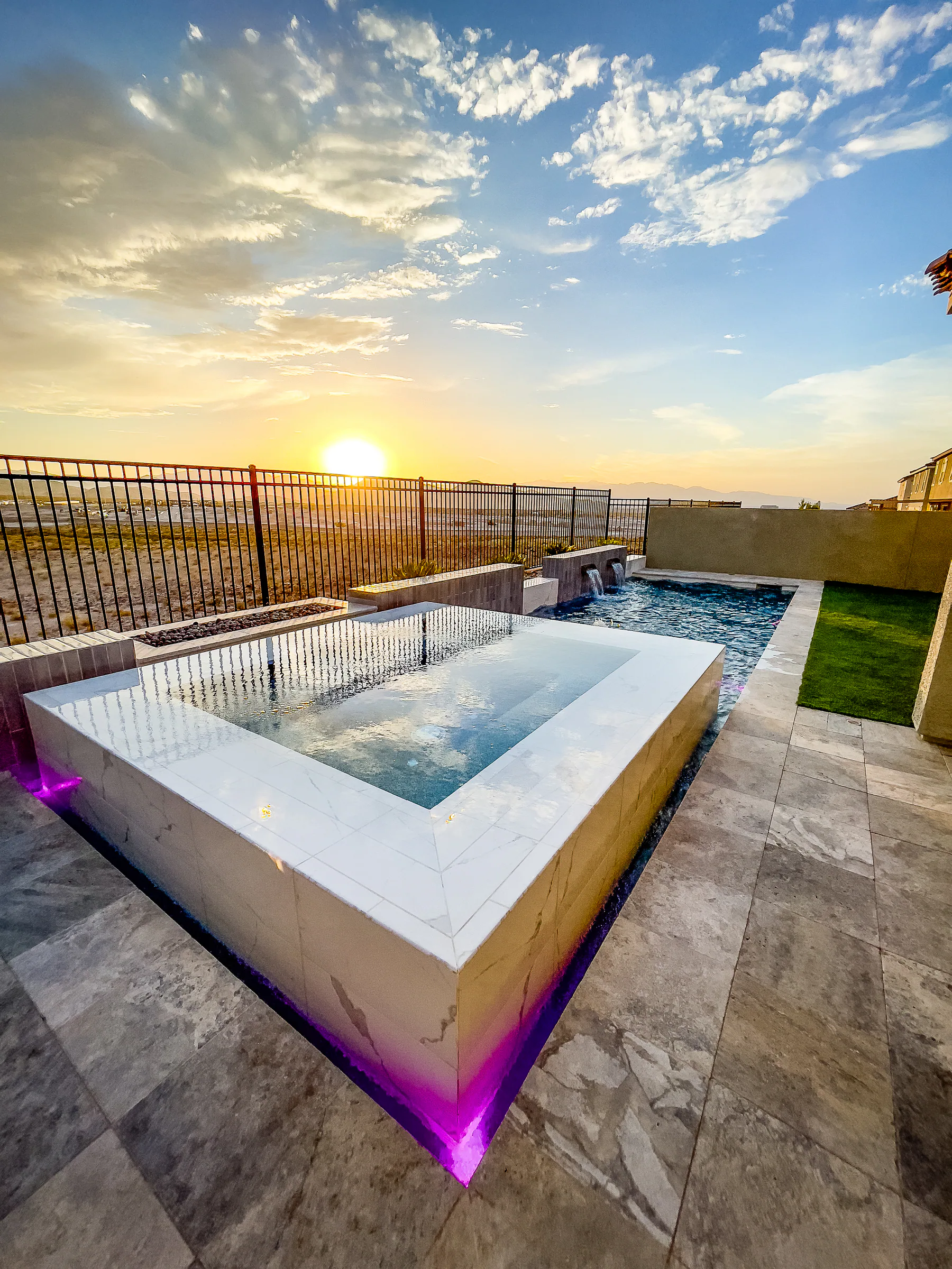 White-tiled raised spa and glass spillover edge reflecting the desert sunset
