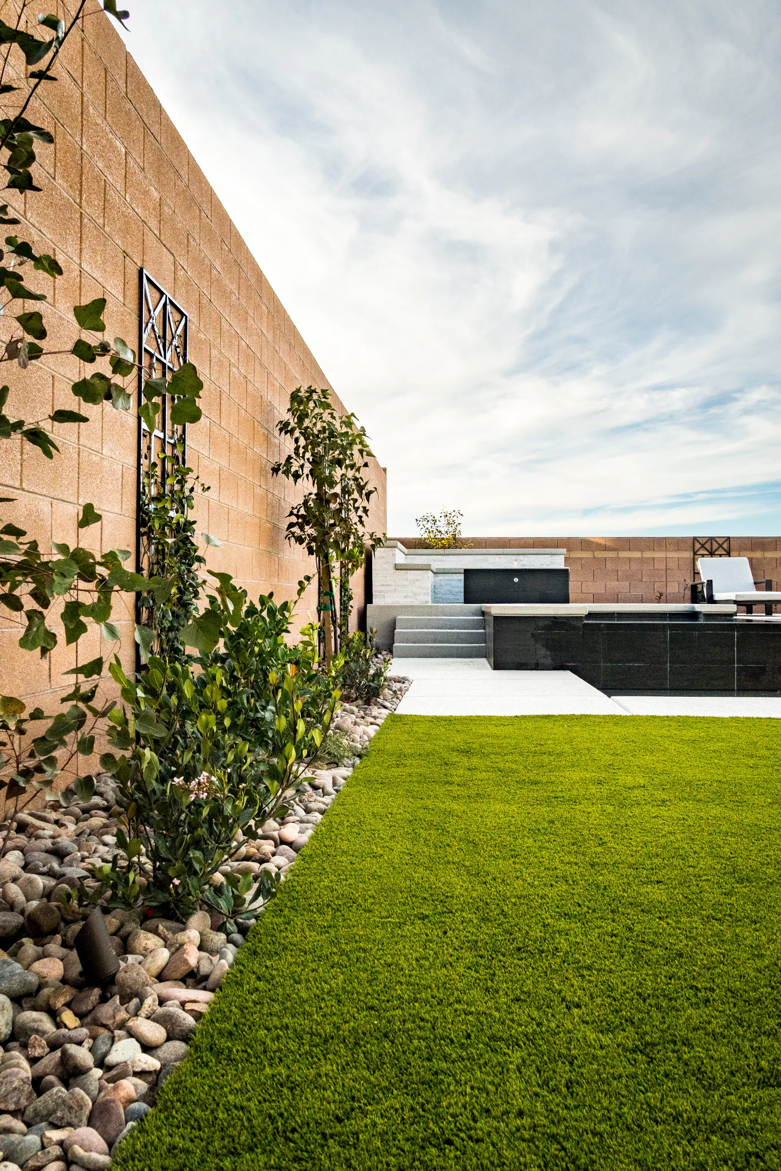 Side yard with artificial turf, river rock, planting, and a trellis