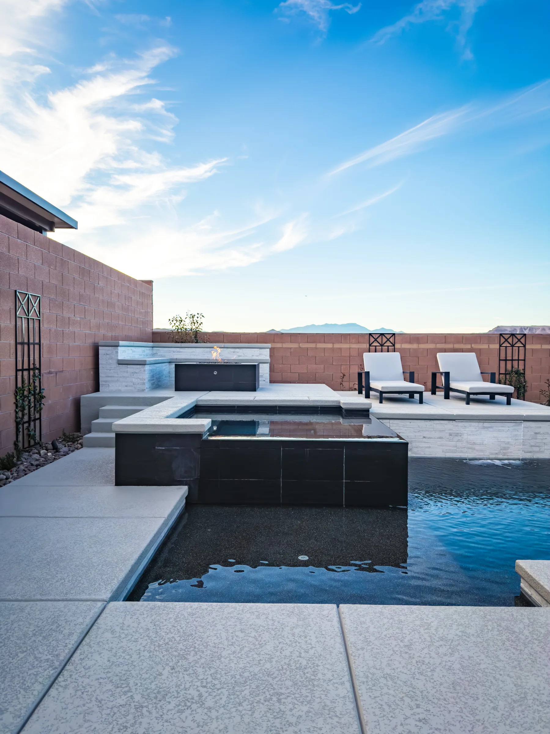 Wide black spa, firepit, and loungers with mountains beyond