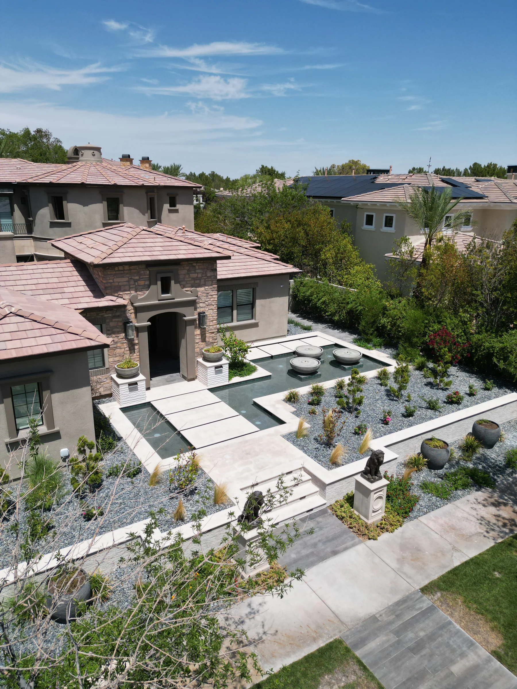Drone view of an entry courtyard with reflecting pools, stone orbs, and desert planting