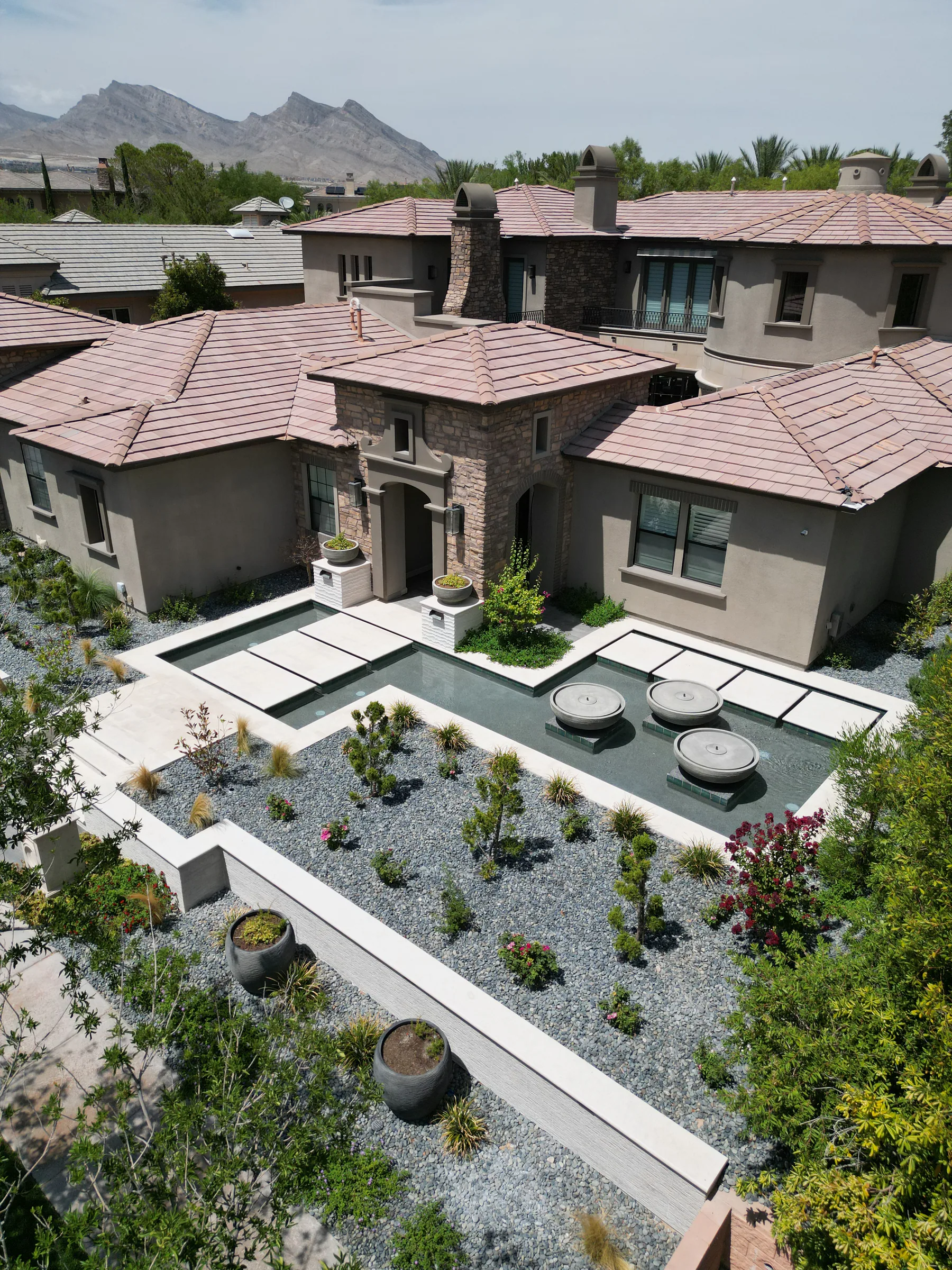 Reflecting pool with stone orbs beside geometric gravel beds, urns, and a mountain view
