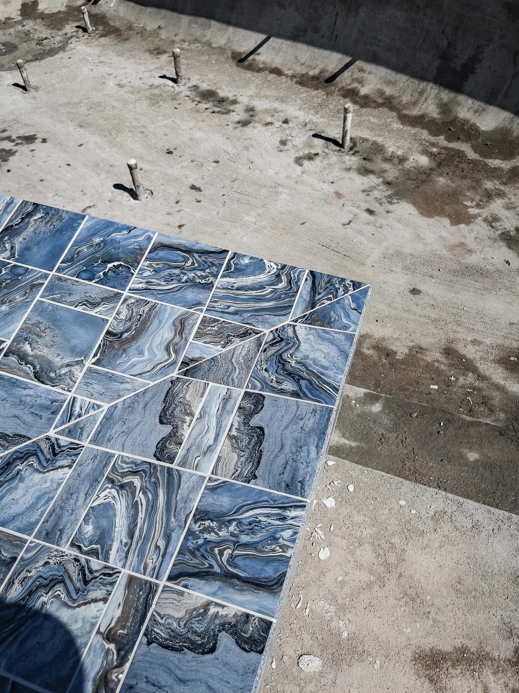 Blue marble-look deck tiles laid beside the pool during construction