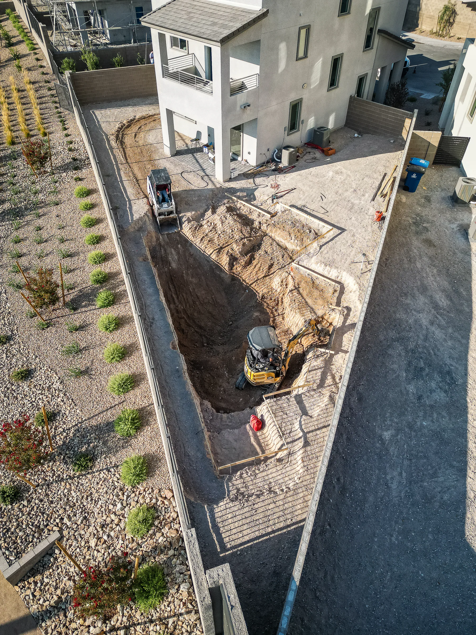Aerial view of excavation underway for a custom pool beside a modern home