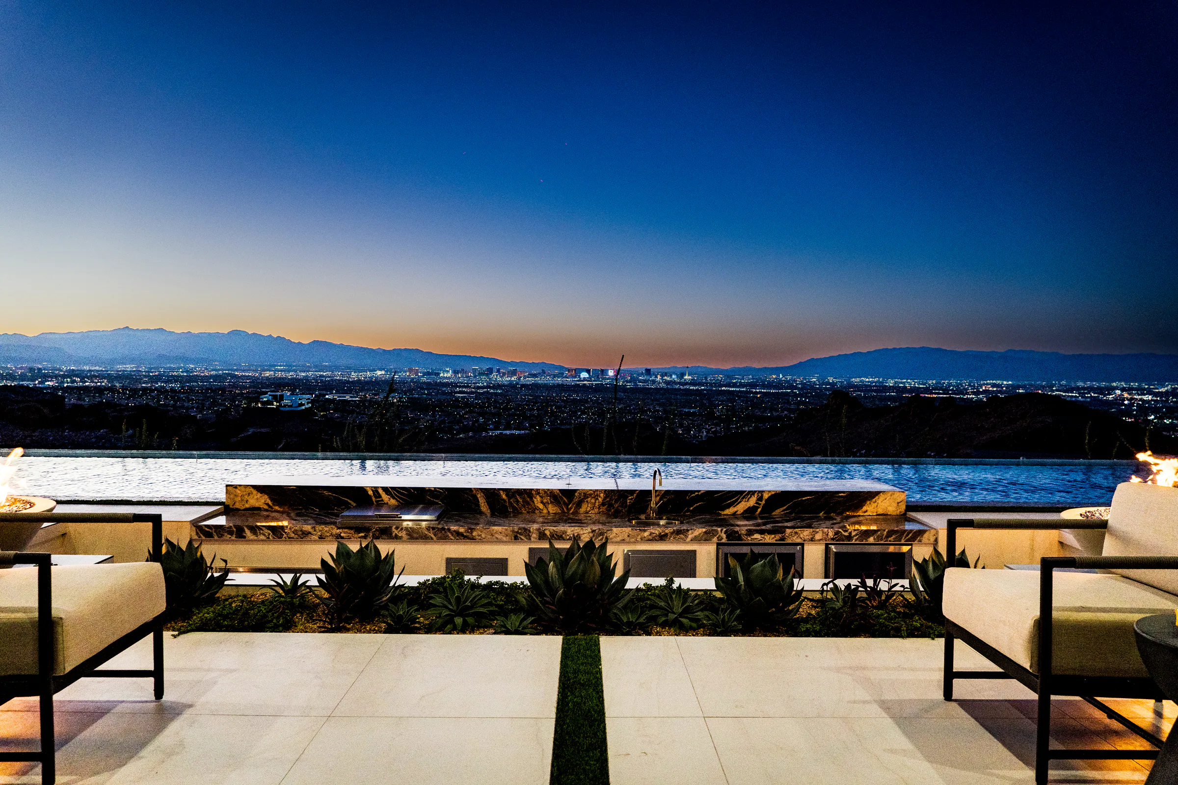 Lounge chairs, agave planting, and a fire feature facing the Las Vegas Strip at dusk