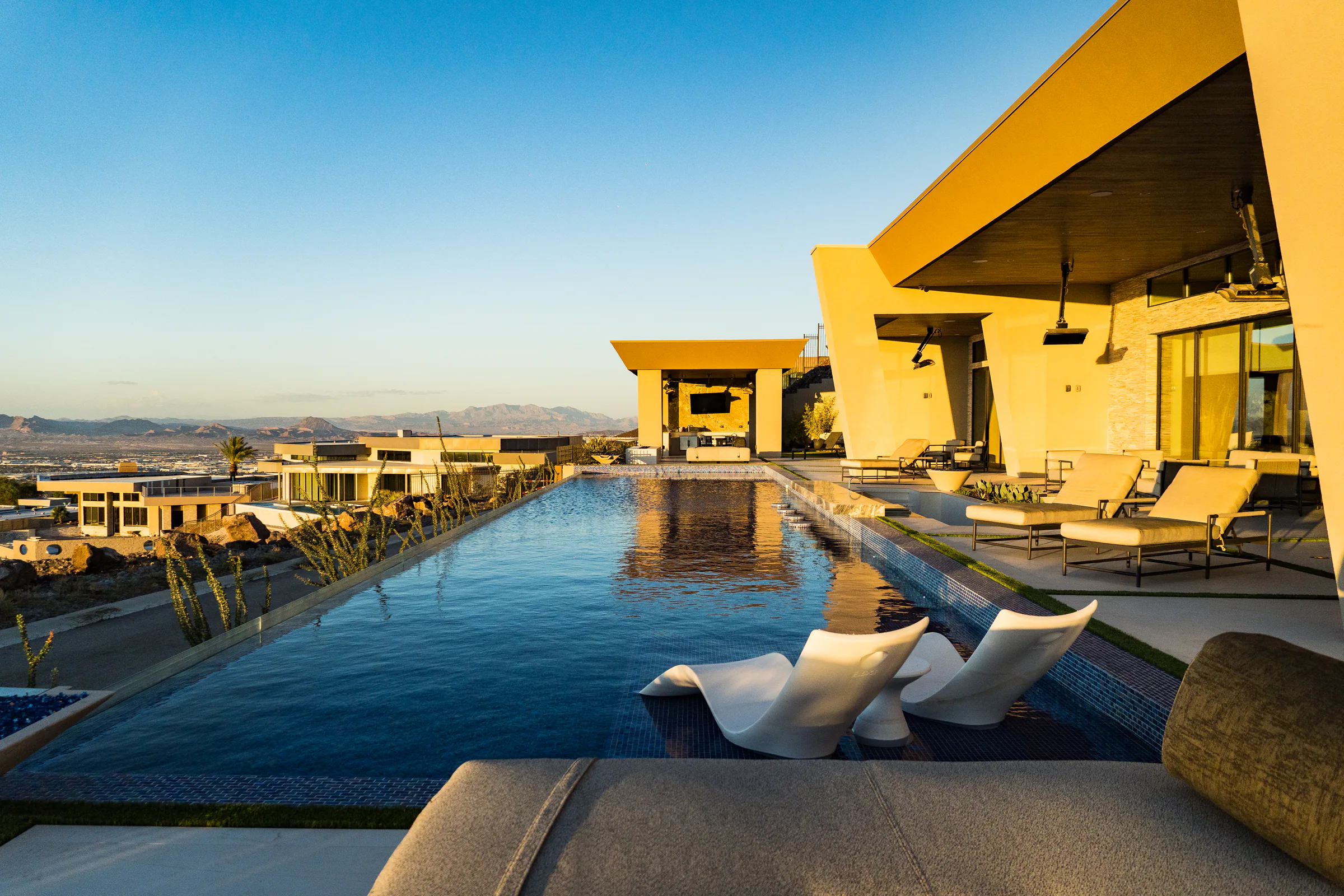 Long infinity-edge pool with in-pool loungers stretching past the home in golden light