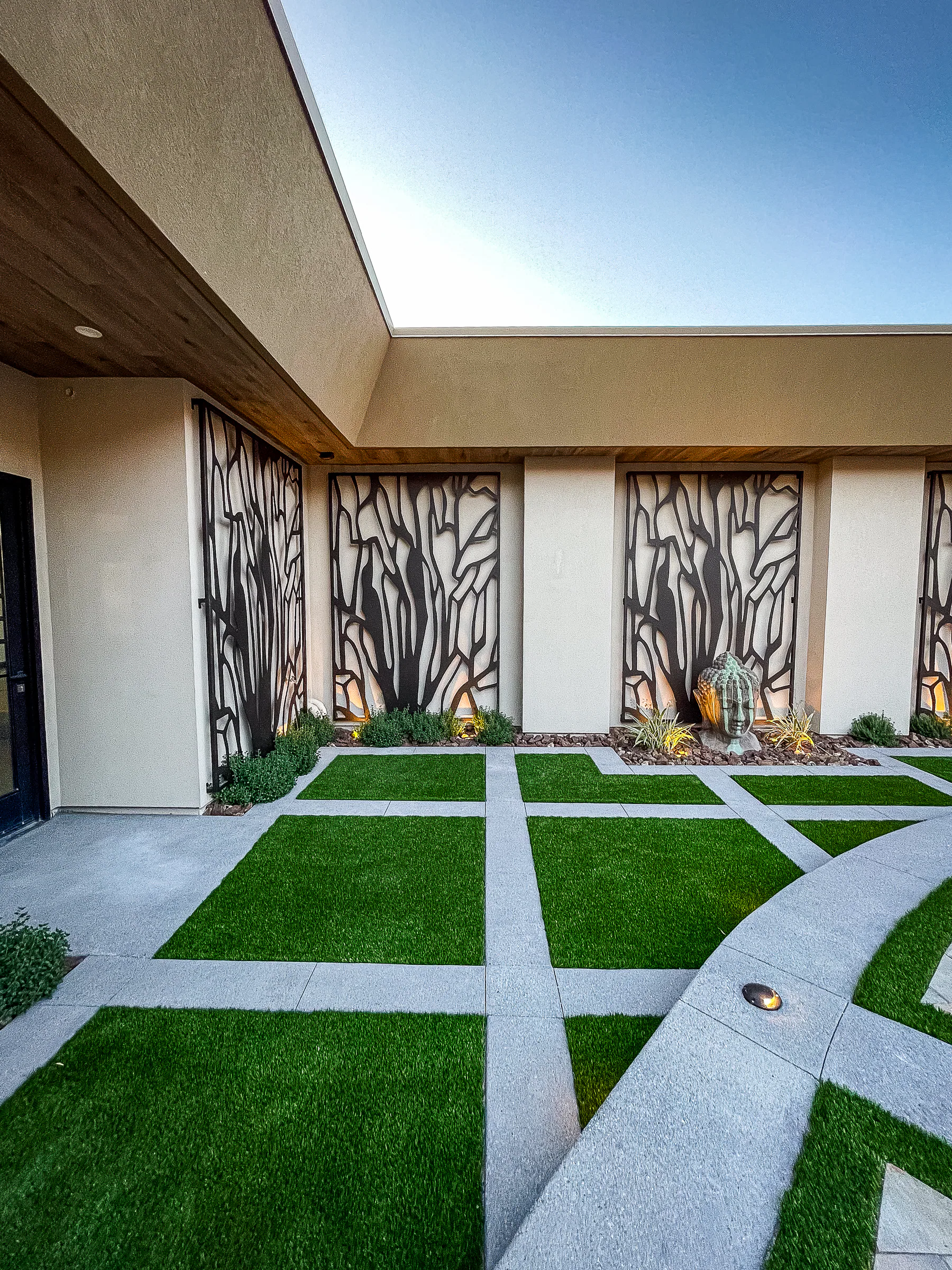 Turf-grid courtyard and custom branch-pattern screens along the modern estate facade