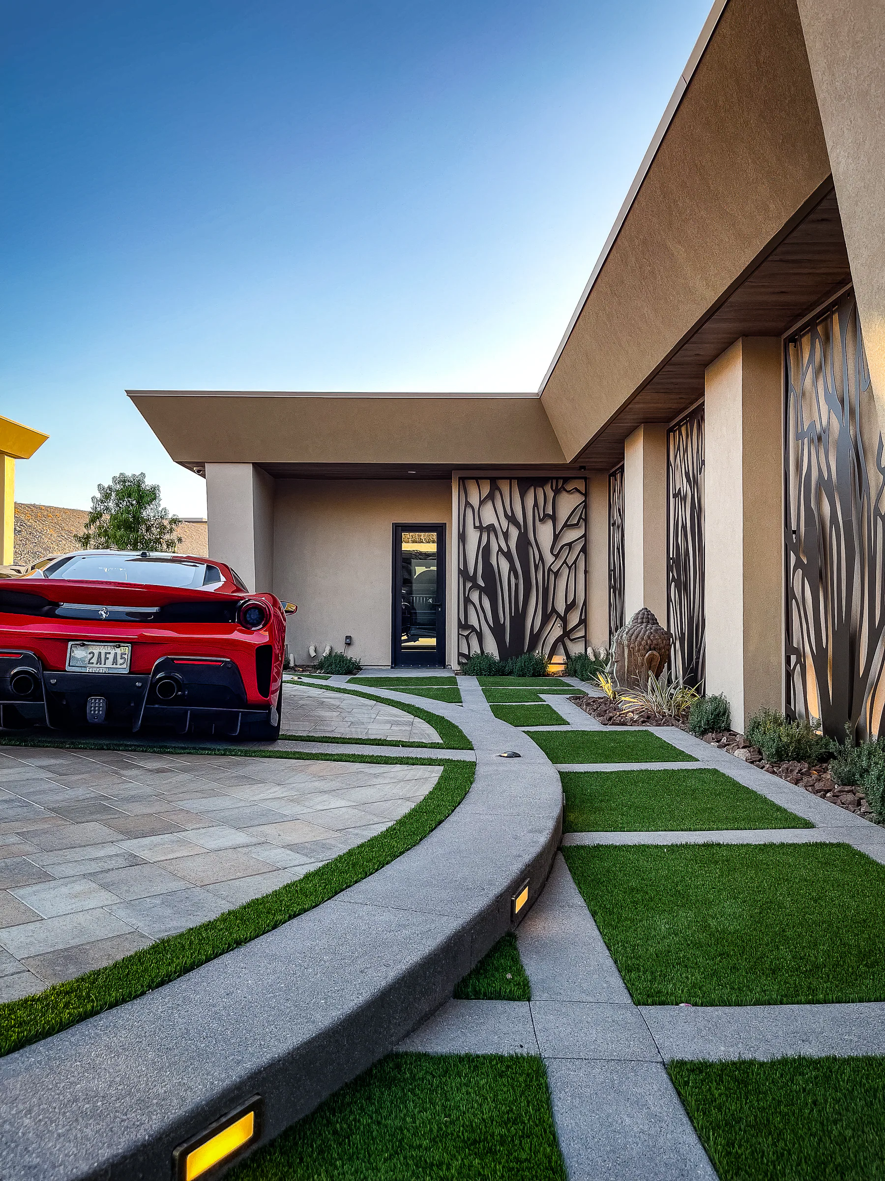 Curved turf-grid driveway leading toward the modern front entry beside a red sports car