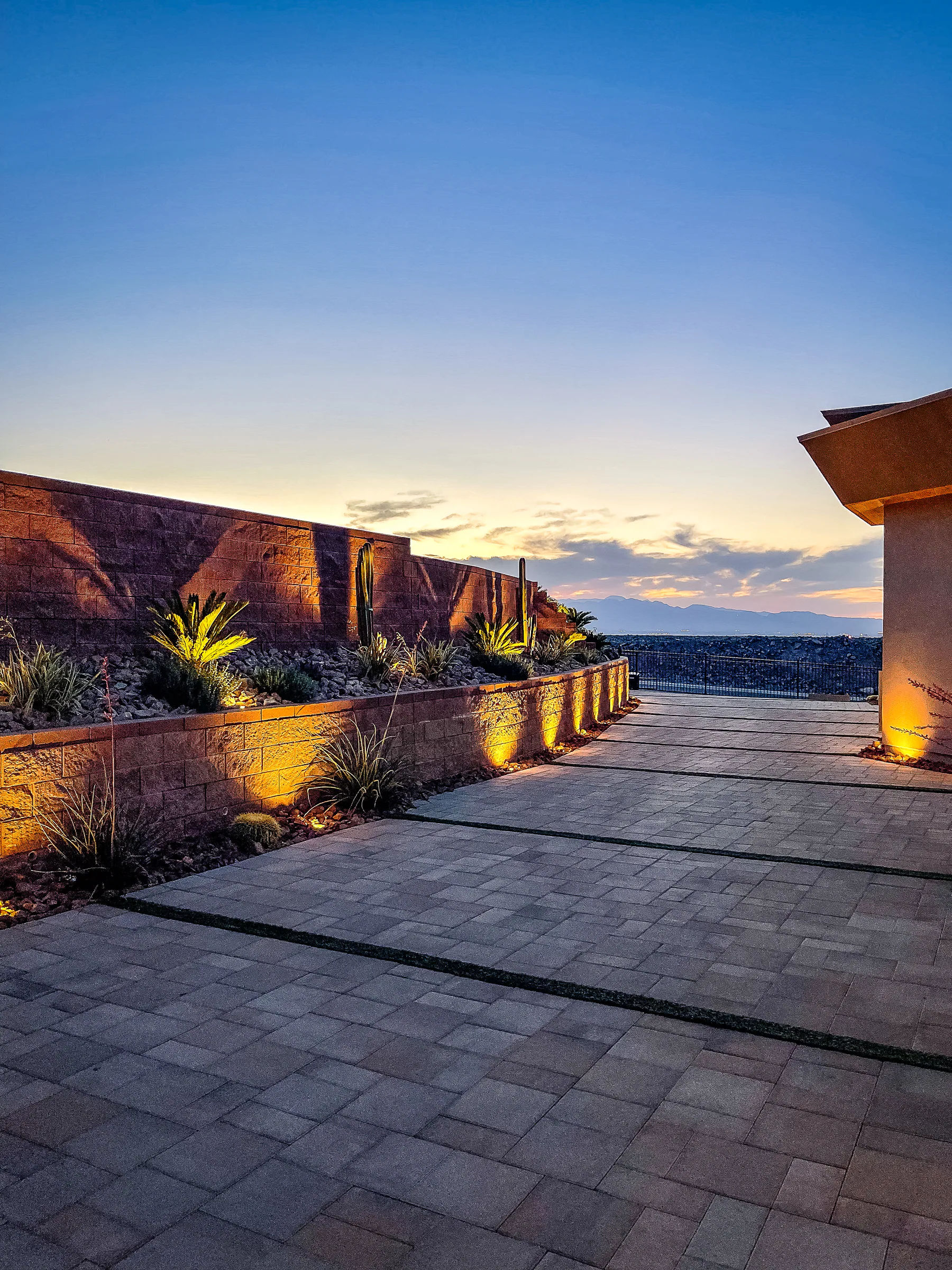Illuminated desert planters lining the paver motor court at sunset