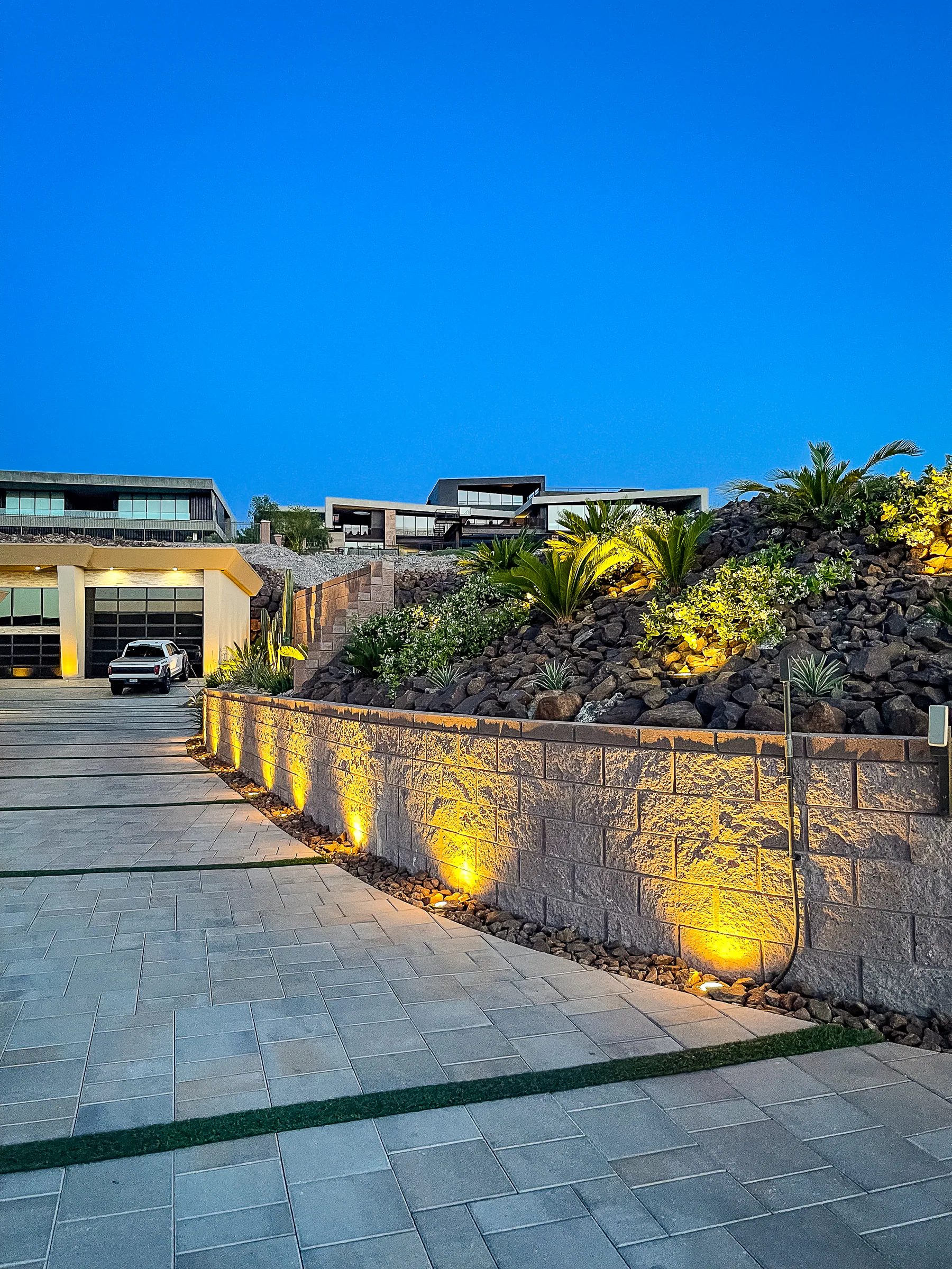 Illuminated terraced desert garden and stone retaining wall beside the motor court